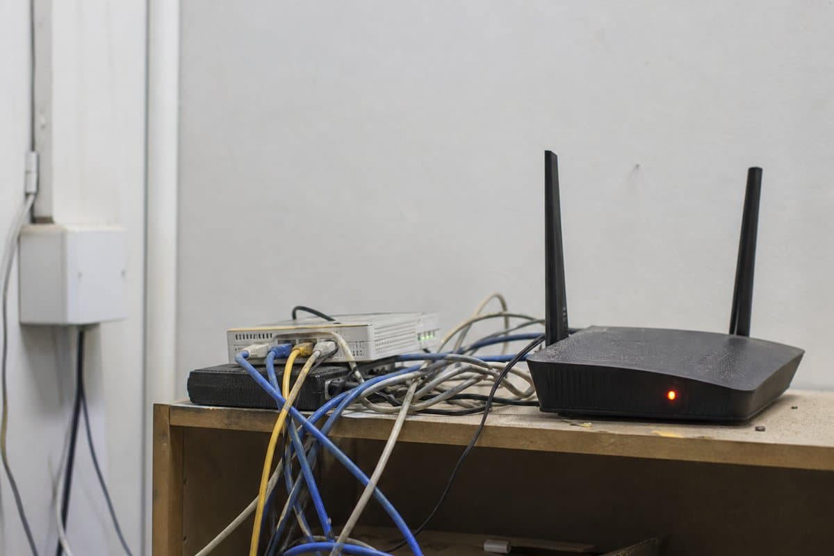 Cluttered shelf with tangled cables and a mismatched old router